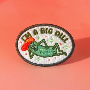 May include: Embroidered oval patch featuring a green pickle in a red hat, with the text "I'M A BIG DILL". The patch has a white background with green star and orange dot accents, and a black border. A fun, quirky design.