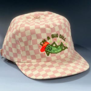 Puede incluir: Gorra de béisbol a cuadros rosas y blancos con la frase bordada "I'm a Big Dill" y un diseño de pepinillo de dibujos animados. La gorra tiene una visera curva y un botón en la parte superior. Un accesorio divertido y juguetón.