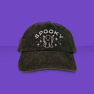 以下が含まれることがあります： 白い刺繍で「SPOOKY」と書いてあり、星と漫画の幽霊が描かれた黒いデニムの野球帽です。