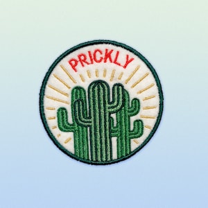 Puede incluir: Un parche redondo bordado blanco con un cactus verde y la palabra "PRICKLY" en letras rojas. El cactus tiene un sol radiante amarillo detr&aacute;s.