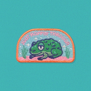 May include: An embroidered patch with a green frog and the text "Just Hoppin' Through" in a pink and orange arch.