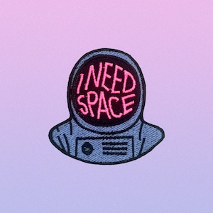 May include: A blue embroidered patch of an astronaut with the text "I NEED SPACE" in pink lettering.
