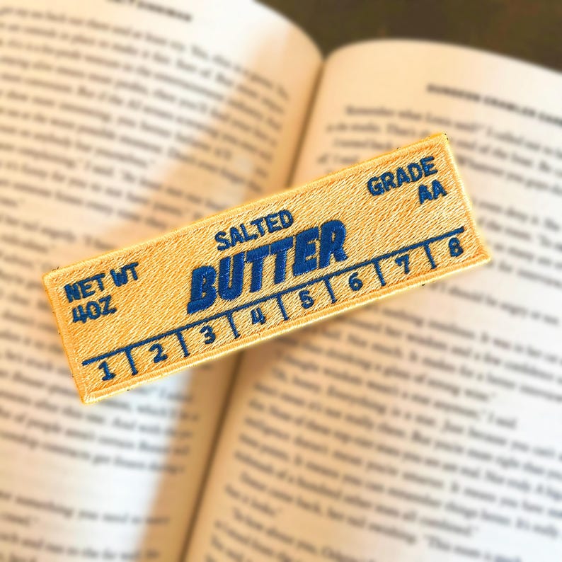 May include: A yellow stick-on patch with blue embroidery that reads "SALTED BUTTER" and has a ruler marked from 1 to 8. The patch also says "NET WT 4OZ" and "GRADE AA".