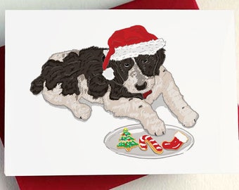 May include: A black and white puppy wearing a red Santa hat looks at a plate of Christmas cookies. The cookies are shaped like a Christmas tree, a candy cane, and a stocking.