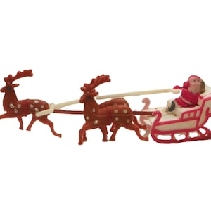 May include: A plastic figurine set featuring a red Santa Claus figure sitting in a white and red sleigh. The sleigh is pulled by three brown reindeer figures with white spots, connected by white plastic harnesses in a linear arrangement.