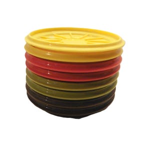 May include: A pile of brightly coloured plastic lids in yellow, gold, red, olive green, and brown. Each lid has a ridged edge and a starburst design in the centre. The lids are stacked on top of each other against a white background.