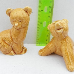 May include: Two ceramic bear figurines, one sitting upright and the other sitting with its head tilted back. Both bears are brown and have a textured surface.