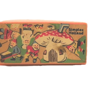 May include: A vintage wooden block with a charming illustration of gnomes and a mushroom house. The block has an orange border and the text "Simplex Holland". The gnomes are shown in different activities, with a red and white mushroom.