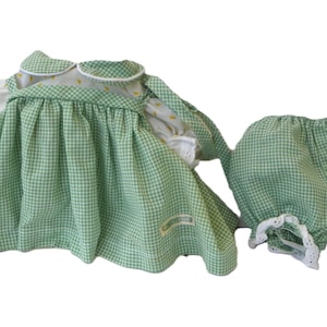 Peut inclure: Une robe à carreaux vichy verts et blancs avec un col blanc et des manches bouffantes ornées d'un petit motif floral jaune, accompagnée d'une culotte bouffante assortie en vichy vert et blanc avec une bordure en dentelle blanche.