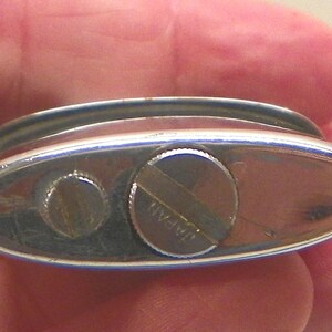 May include: An oval-shaped silver-toned metal lighter base featuring a smooth, reflective surface. The base includes two circular screw-in components, with the larger one clearly engraved with the word JAPAN across its center surface.