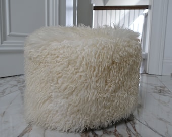 May include: A white fluffy round ottoman or pouf sits on a marble floor.