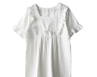 May include: White cotton nightgown with lace trim and ruffled edges. The neckline features a V-shape with a bow detail.