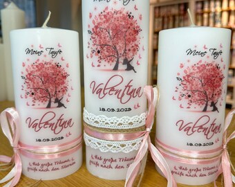May include: Three white candles with pink and white floral designs and the text "Meine Taufe" and "Valentyn" with the date "18.03.2023". Each candle is decorated with a pink and white ribbon and a burlap bow.