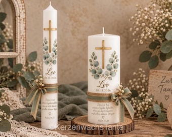 Könnte beinhalten: Zwei weiße zylindrische Kerzen mit einem goldenen Kreuz, grünen Eukalyptusblättern, dem Namen Leo, dem Datum 08.11.2026 und einem deutschen Text aus Psalm 91,11. Jede Kerze ist mit einem grünen Band, einer kleinen Schleife und Schleierkraut verziert.