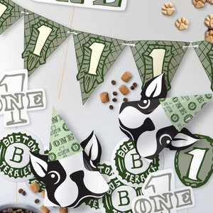 Puede incluir: Decoraciones de fiesta verdes y blancas para un primer cumpleaños, que incluyen una pancarta, un sombrero y un adorno para pastel. Las decoraciones presentan el número uno y las palabras "Boston Terrier" y "One".