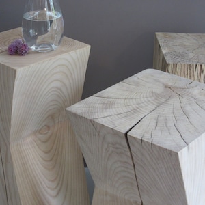 May include: Three wooden stools with a unique, geometric design. The stools are made of light-coloured wood and have a natural, rustic finish.