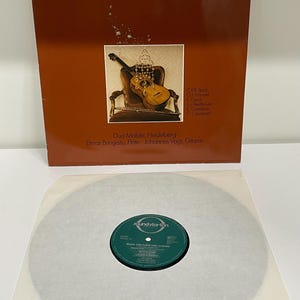 Può includere: Un album in vinile vintage intitolato "Musik für Flöte und Gitarre". La copertina è marrone con testo bianco e un'immagine di una chitarra e un flauto. Il disco è visibile sotto, con un'etichetta verde.