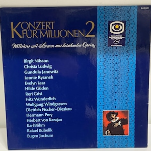 May include: A vintage vinyl record album cover, predominantly navy blue, featuring the title "Konzert Für Millionen 2" in large gold lettering. The cover lists opera stars and includes a small portrait of a man in a hat. The album is a Deutsche Grammophon release.
