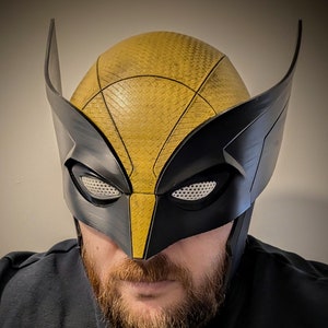 May include: A black and yellow Wolverine mask with a mesh eye covering. The mask is made of a hard plastic material and has a textured surface.