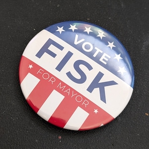 May include: A blue and red button with white stars and the text "Vote Fisk for Mayor".