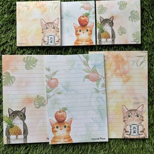 May include: Set of six stationery notepads featuring adorable illustrations of cats with various accessories, including an apple, pineapple, and a cup of tea. The notepads have a watercolor background with a light blue and orange color scheme. The notepads are perfect for writing letters, notes, or reminders.