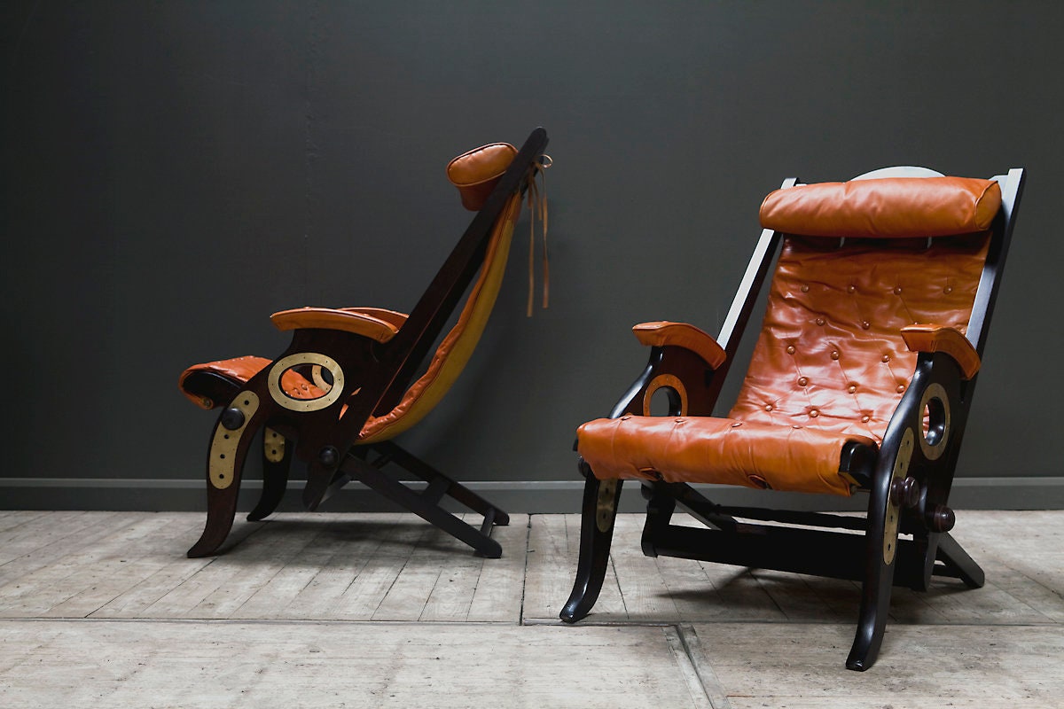 Photo of two folding chairs with brown leather backs, and dark wood structures.