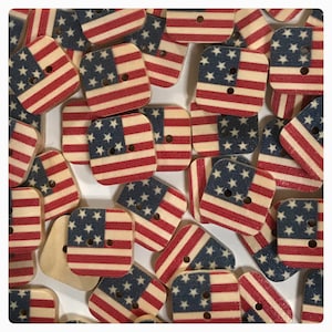 May include: A collection of wooden buttons with an American flag design. The buttons are square shaped and have a distressed look.