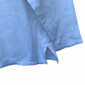 May include: A light blue sweatshirt with a split hem detail at the bottom. The fabric appears soft and has a slight texture. The image is a close-up of the garment's hem and sleeve.