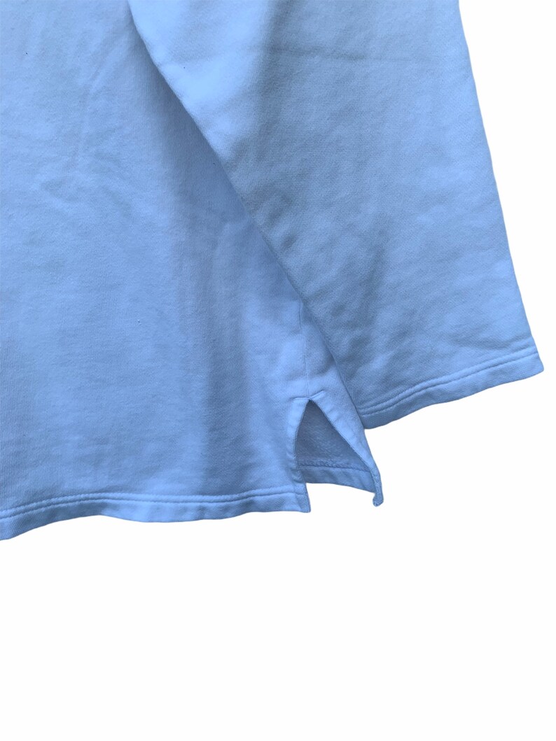 May include: A light blue sweatshirt with a split hem detail at the bottom. The fabric appears soft and has a slight texture. The image is a close-up of the garment's hem and sleeve.