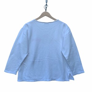 May include: A white long-sleeve shirt with a scoop neck and side slits. The shirt is hanging on a wooden hanger suspended by a metal chain. The shirt is made of a soft, lightweight material.
