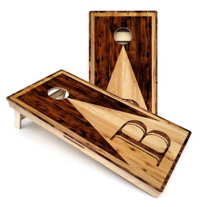 May include: A wooden cornhole game set with a triangular design and the letter "B" in the center. The boards are made of different types of wood, creating a unique and rustic look.