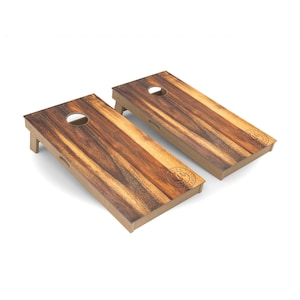 May include: Two wooden cornhole boards with a brown wood grain finish. Each board has a circular hole in the center and a logo with the text "Game On" printed on the surface.