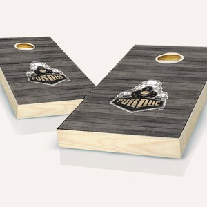 May include: A set of two wooden cornhole boards with a gray wood grain design. The boards feature a Purdue University logo with the text "Purdue" in gold lettering.