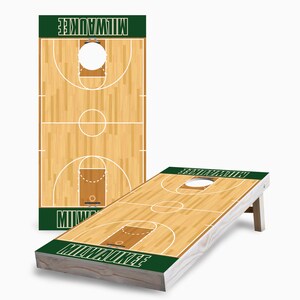 May include: A wooden cornhole game with a basketball court design. The boards are painted with a brown wood grain pattern and have a green stripe at the bottom with the word "MILWAUKEE" in white letters. The boards have a white basketball court design with a white circle in the center of each board.