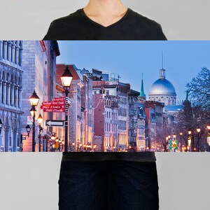 Puede incluir: Una vista panor&aacute;mica de una calle en Montreal, Quebec, Canad&aacute; al atardecer. La calle est&aacute; bordeada de edificios hist&oacute;ricos y farolas. La Bas&iacute;lica de Notre-Dame es visible en la distancia.