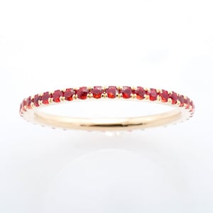 May include: A thin gold band ring with a row of small red gemstones set around the entire band.