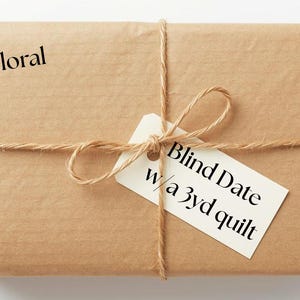 May include: A parcel wrapped in brown paper, secured with twine and a tag. The tag says "Blind Date w/ a 3yd quilt". The word "Floral" is printed on the package. The background is white.