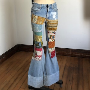 May include: Blue denim bell bottom jeans with patchwork details in various colors and patterns, including floral, paisley, and geometric designs.