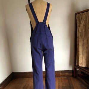 K&ouml;nnte beinhalten: Eine blaue Denim-Latzhose mit verstellbaren Tr&auml;gern. Die Latzhose hat weite Beine und eine Ges&auml;&szlig;tasche.