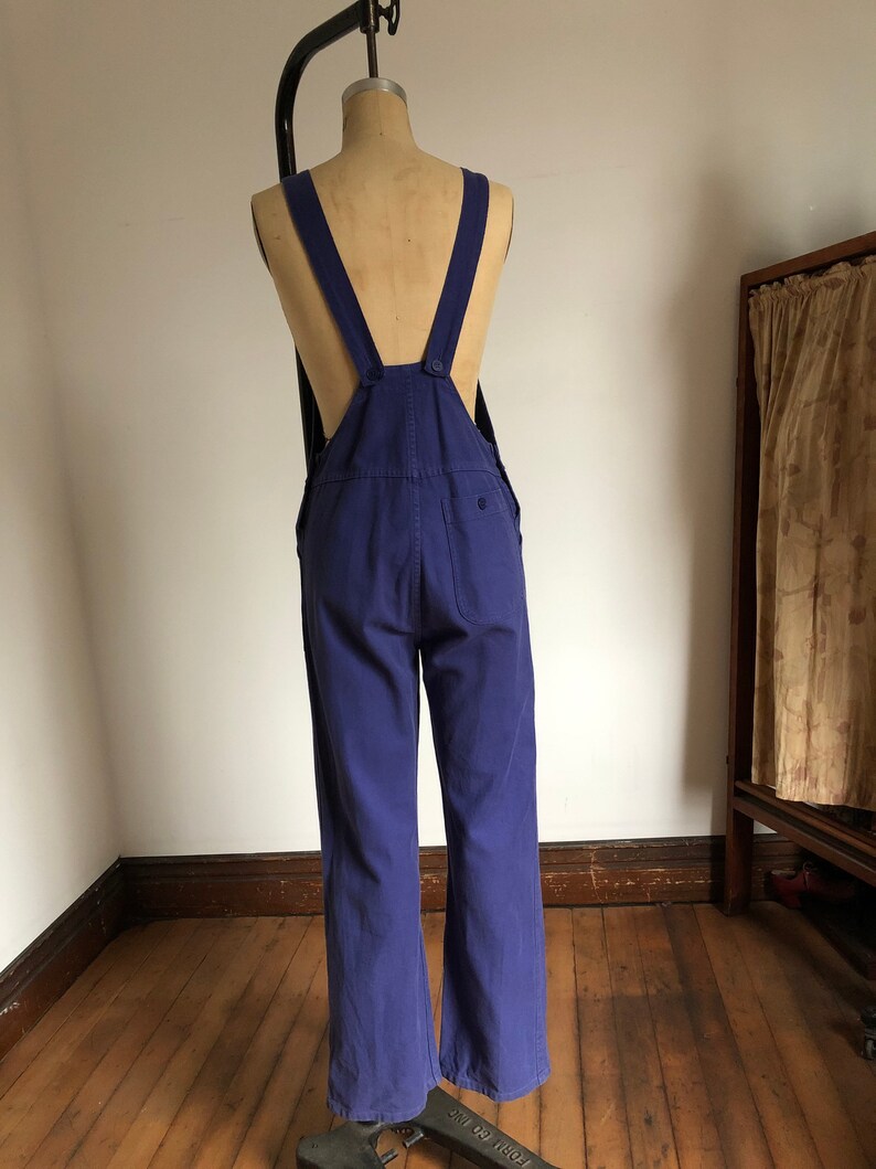 K&ouml;nnte beinhalten: Eine blaue Denim-Latzhose mit verstellbaren Tr&auml;gern. Die Latzhose hat weite Beine und eine Ges&auml;&szlig;tasche.