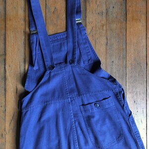 K&ouml;nnte beinhalten: Eine blaue Denim-Latzhose mit verstellbaren Tr&auml;gern und einer einzigen Ges&auml;&szlig;tasche.
