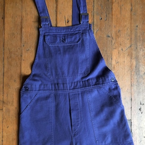 K&ouml;nnte beinhalten: Eine blaue Denim-Latzhose mit verstellbaren Tr&auml;gern und mehreren Taschen.