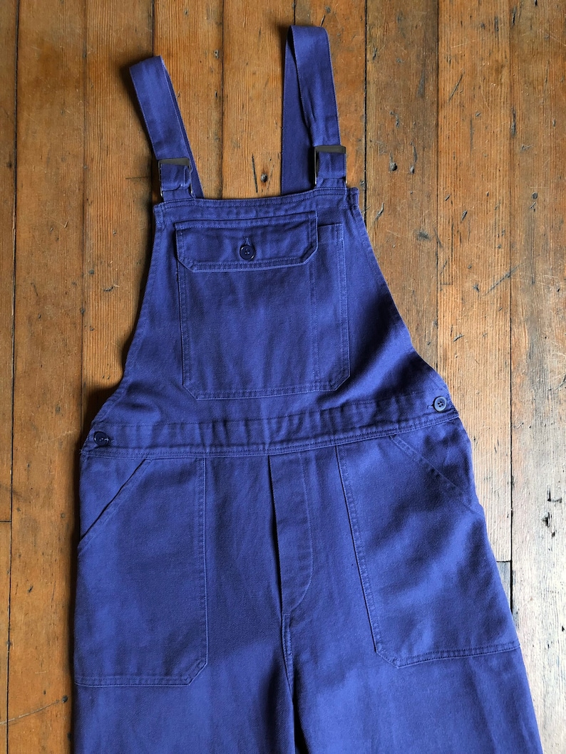 K&ouml;nnte beinhalten: Eine blaue Denim-Latzhose mit verstellbaren Tr&auml;gern und mehreren Taschen.