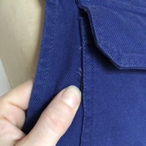 K&ouml;nnte beinhalten: Nahaufnahme eines dunkelblauen Jeansstoffes mit einer einzigen Naht, die vertikal in der Mitte verl&auml;uft. Der Stoff hat eine subtile Textur und einen leichten Glanz.