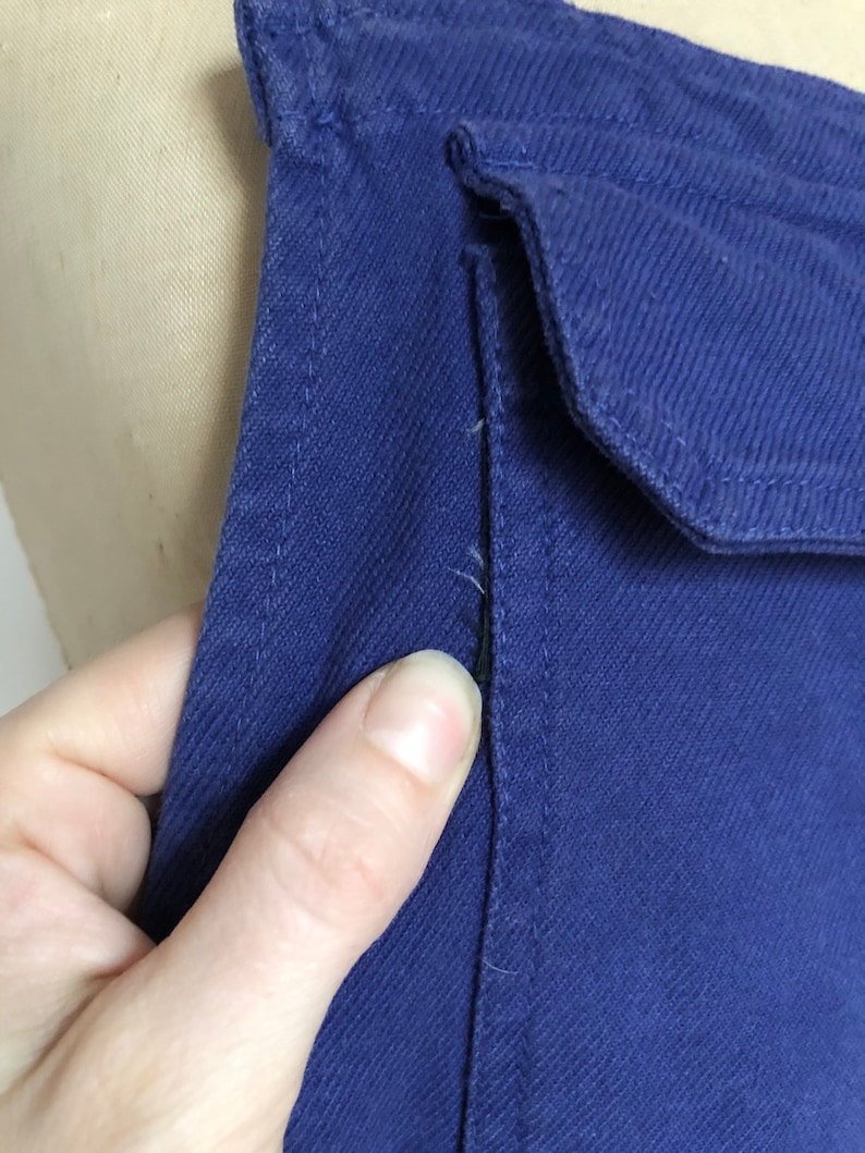 K&ouml;nnte beinhalten: Nahaufnahme eines dunkelblauen Jeansstoffes mit einer einzigen Naht, die vertikal in der Mitte verl&auml;uft. Der Stoff hat eine subtile Textur und einen leichten Glanz.