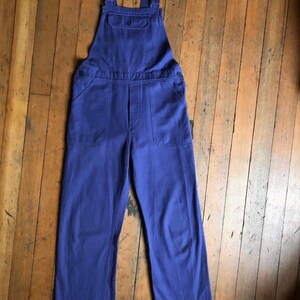K&ouml;nnte beinhalten: Eine blaue Latzhose aus Denim mit verstellbaren Tr&auml;gern und einer gro&szlig;en Tasche vorne.