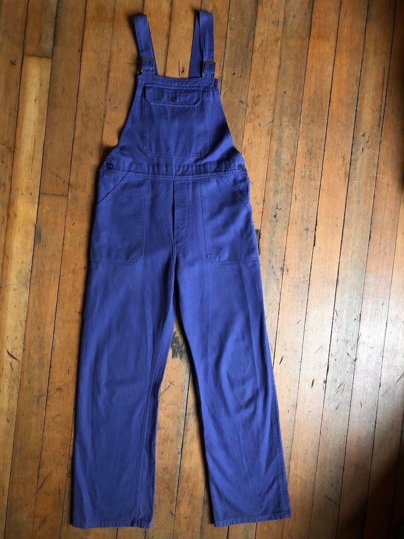 K&ouml;nnte beinhalten: Eine blaue Latzhose aus Denim mit verstellbaren Tr&auml;gern und einer gro&szlig;en Tasche vorne.