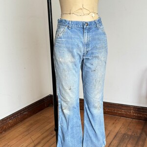 May include: Light blue denim jeans with a faded wash and slight distressing. The jeans have a classic five-pocket design and a flared leg. The jeans are displayed on a mannequin.