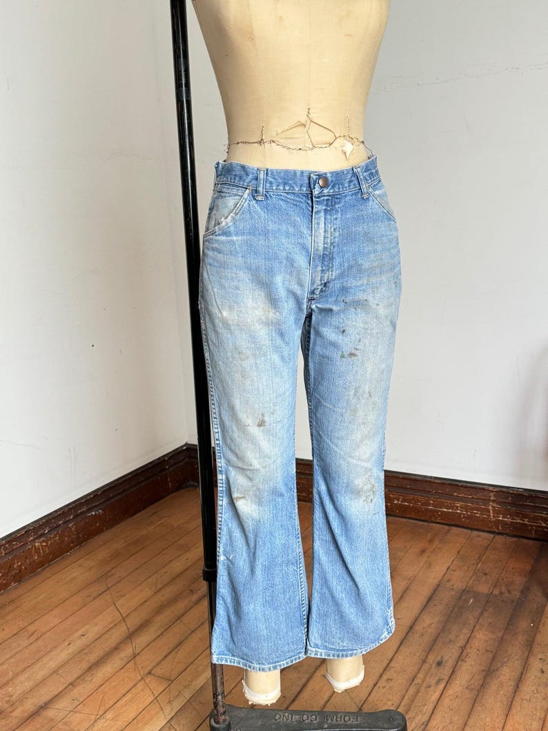 May include: Light blue denim jeans with a faded wash and slight distressing. The jeans have a classic five-pocket design and a flared leg. The jeans are displayed on a mannequin.