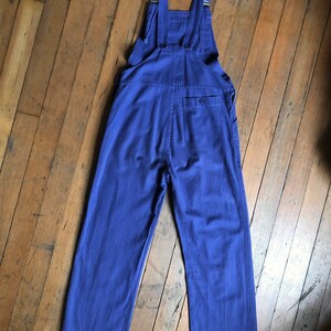 K&ouml;nnte beinhalten: Eine blaue Denim-Latzhose mit verstellbaren Tr&auml;gern und einer einzigen Ges&auml;&szlig;tasche.